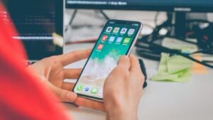 person holding iphone, which is showing the home screen  