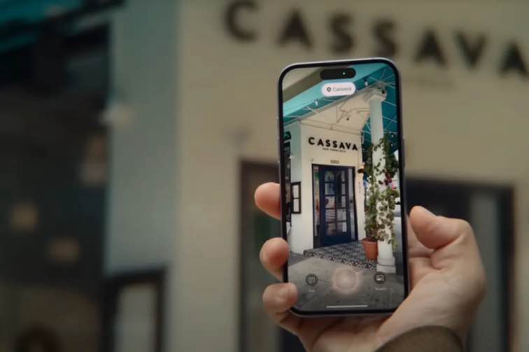 A person using Visual Intelligence from Apple’s iPhone 16 announcement video. The person is holding their iPhone in front of a restaurant and looking at what’s shown onscreen.